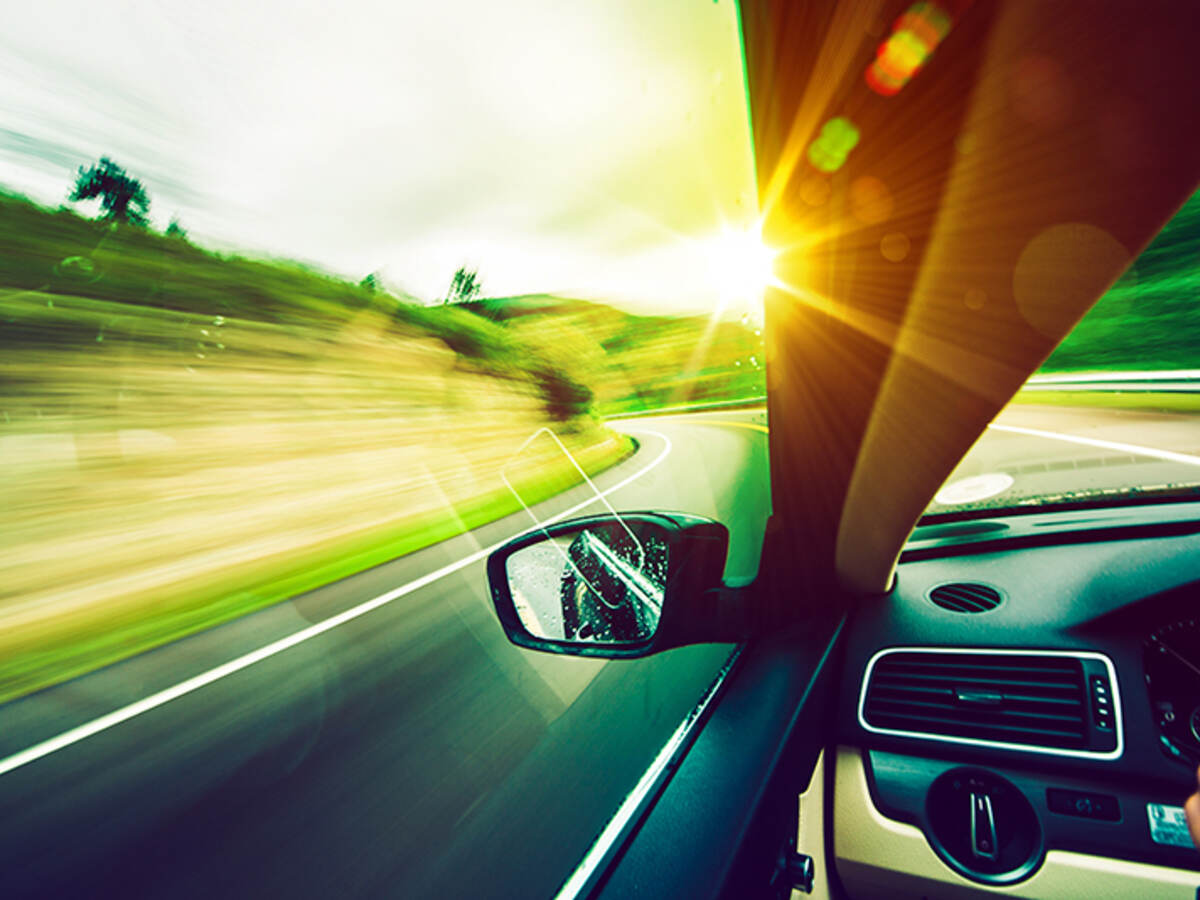 View out of a car on a road with sunlight by left side of the windshield