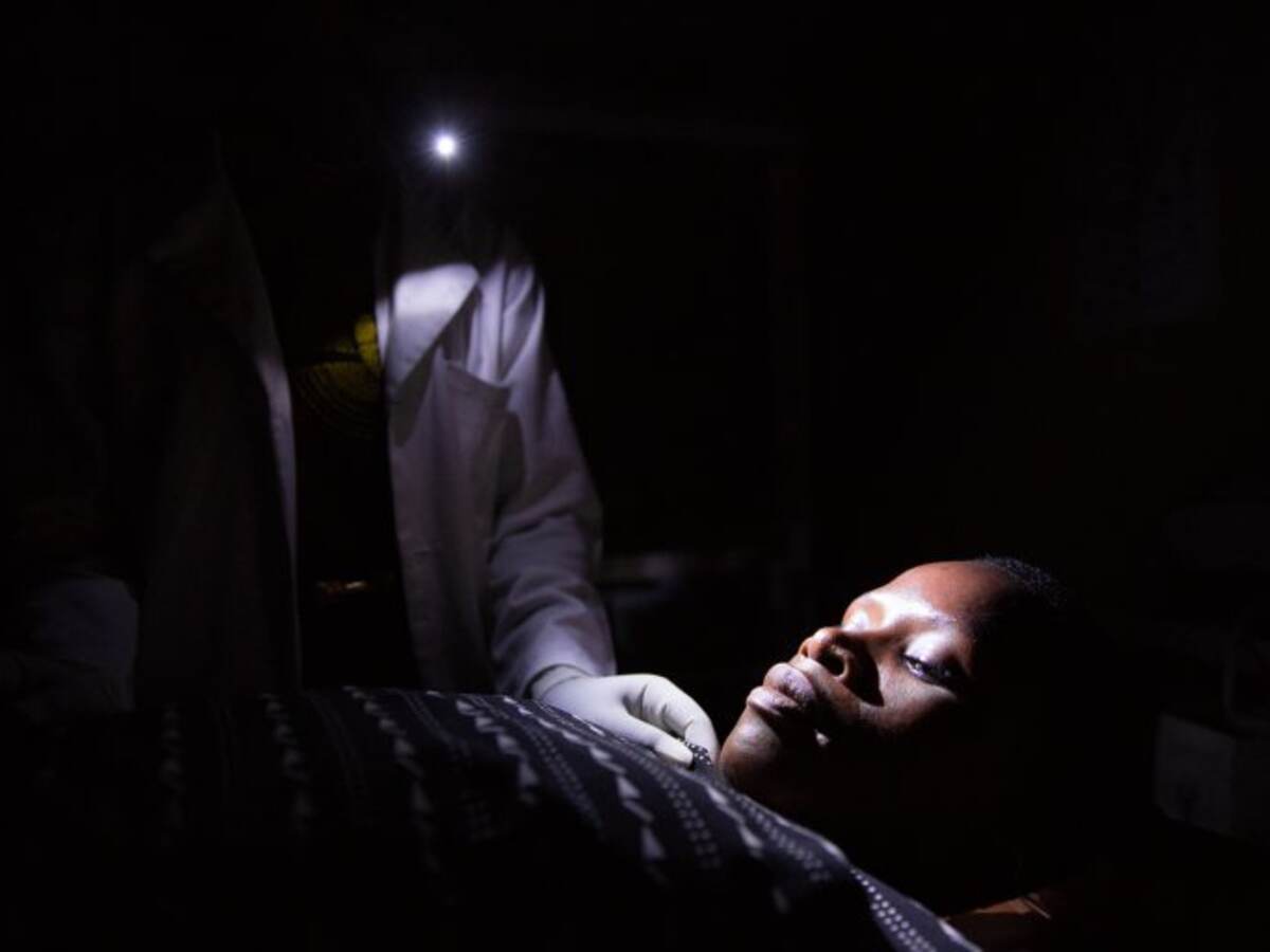 Tanzania midwife at night holding cellphone light over female patient