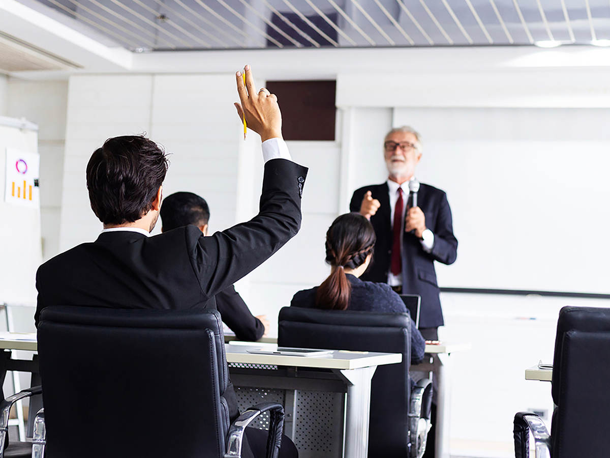 Business man raising hand in a classroom setting