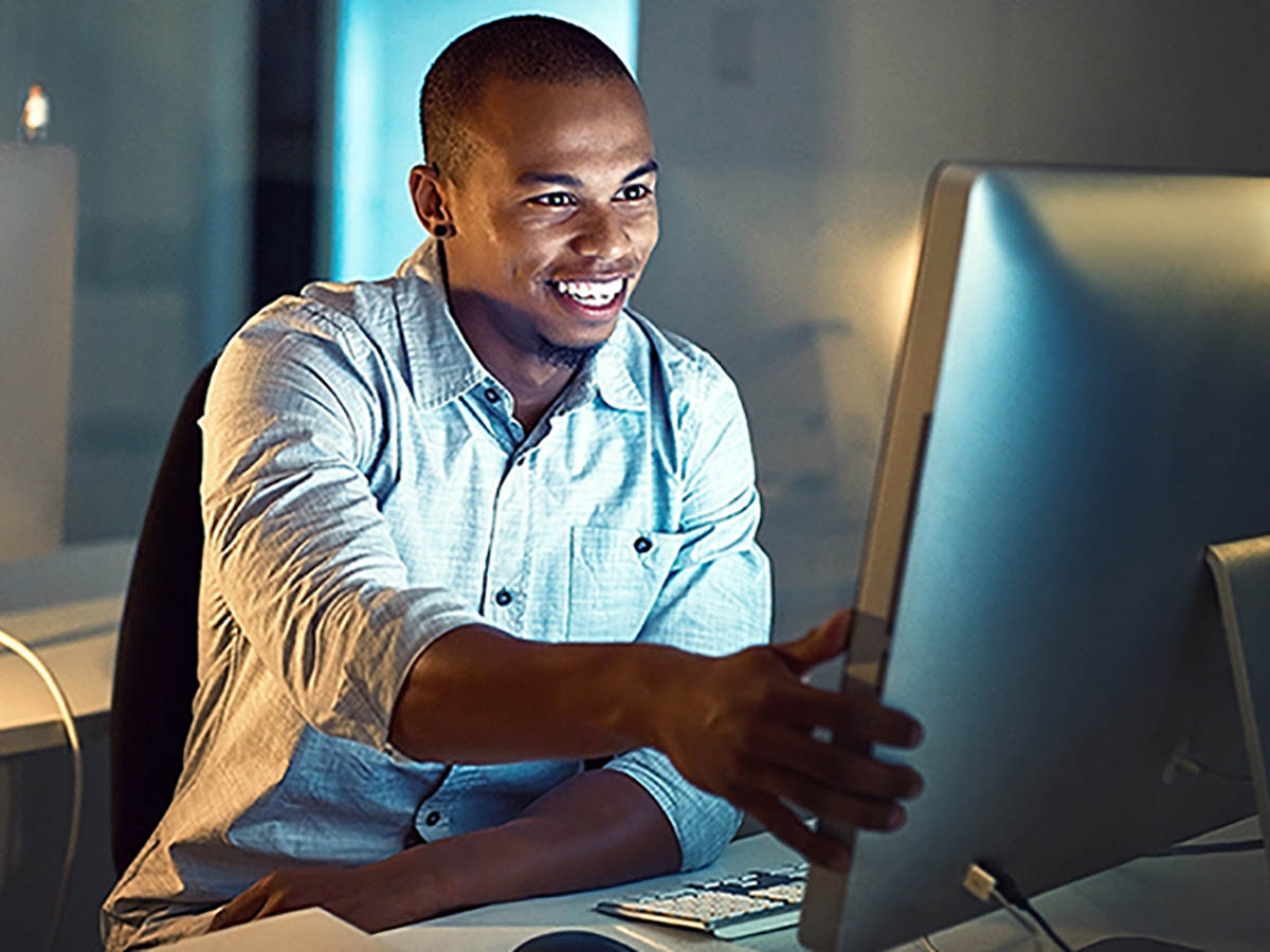 Smiling man sitting at a desk in front of a computer monitor