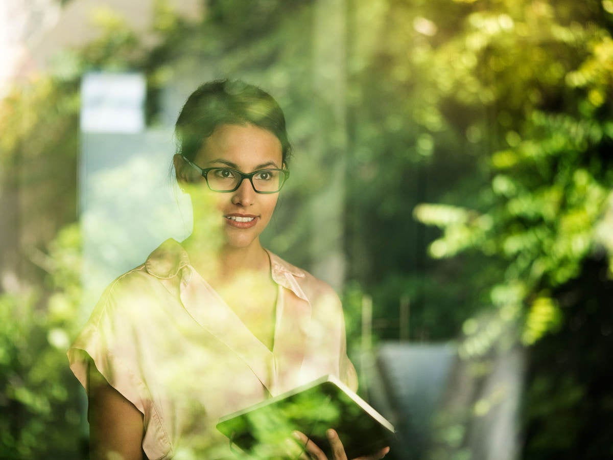 A woman stands at a window with reflected greenery.