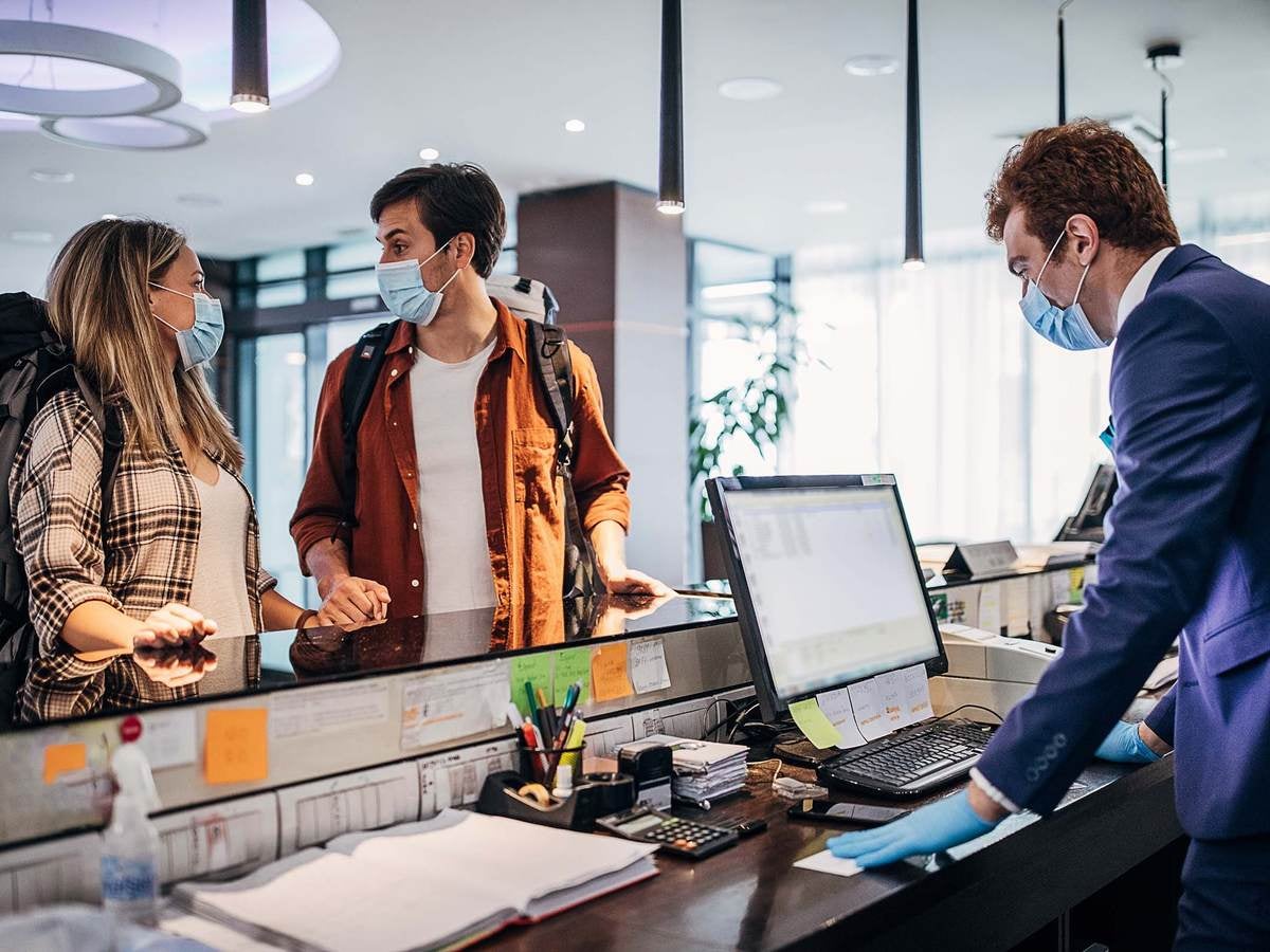 Hotel guests and staff wearing proper personal protective equipment at hotel reception