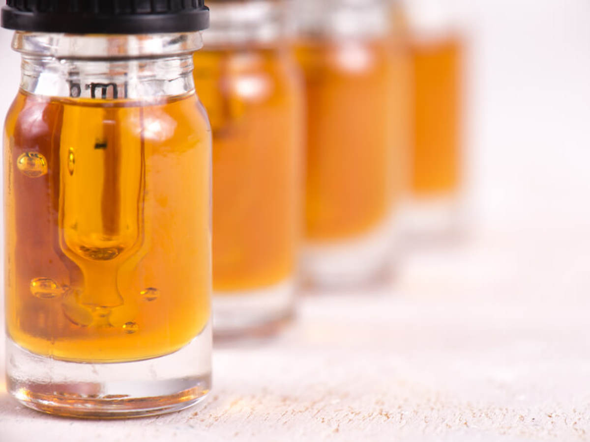 Small vials of golden CBD oil lined up on an austere white background.