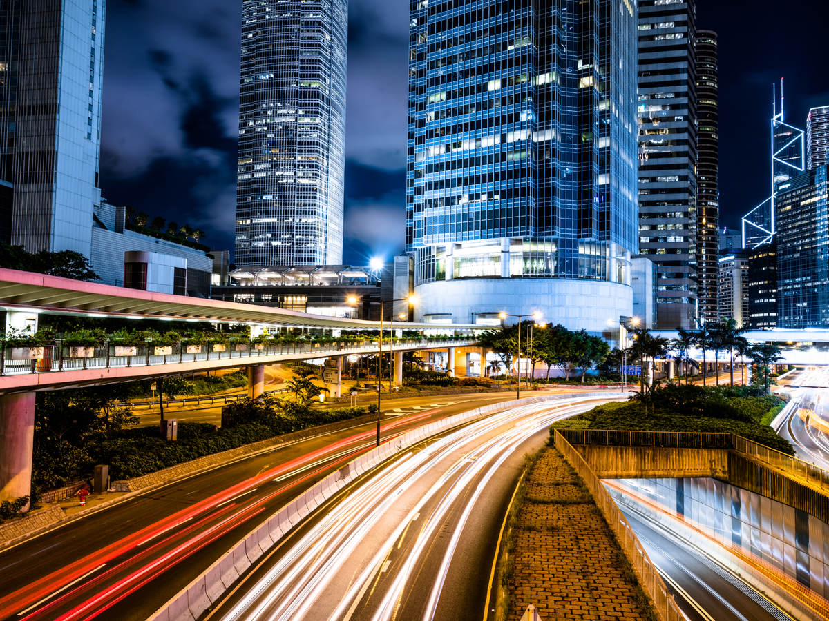 A multi-lane highway is brightly illuminated by roadway lighting, with a modern cityscape on the horizon.