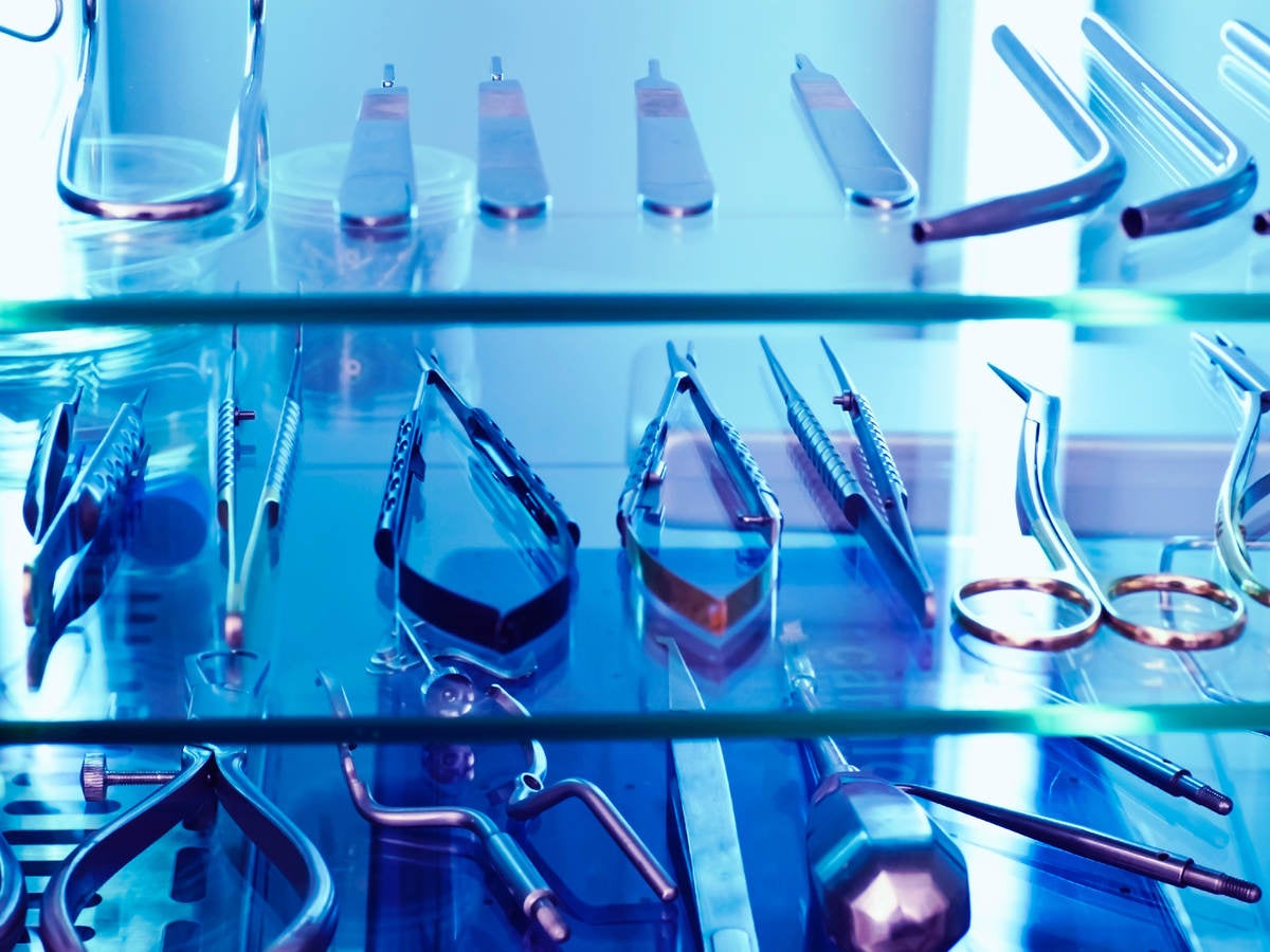 Medical tools sit on a shelf under the blue glow of ultraviolet light, used as a germicidal disinfectant.