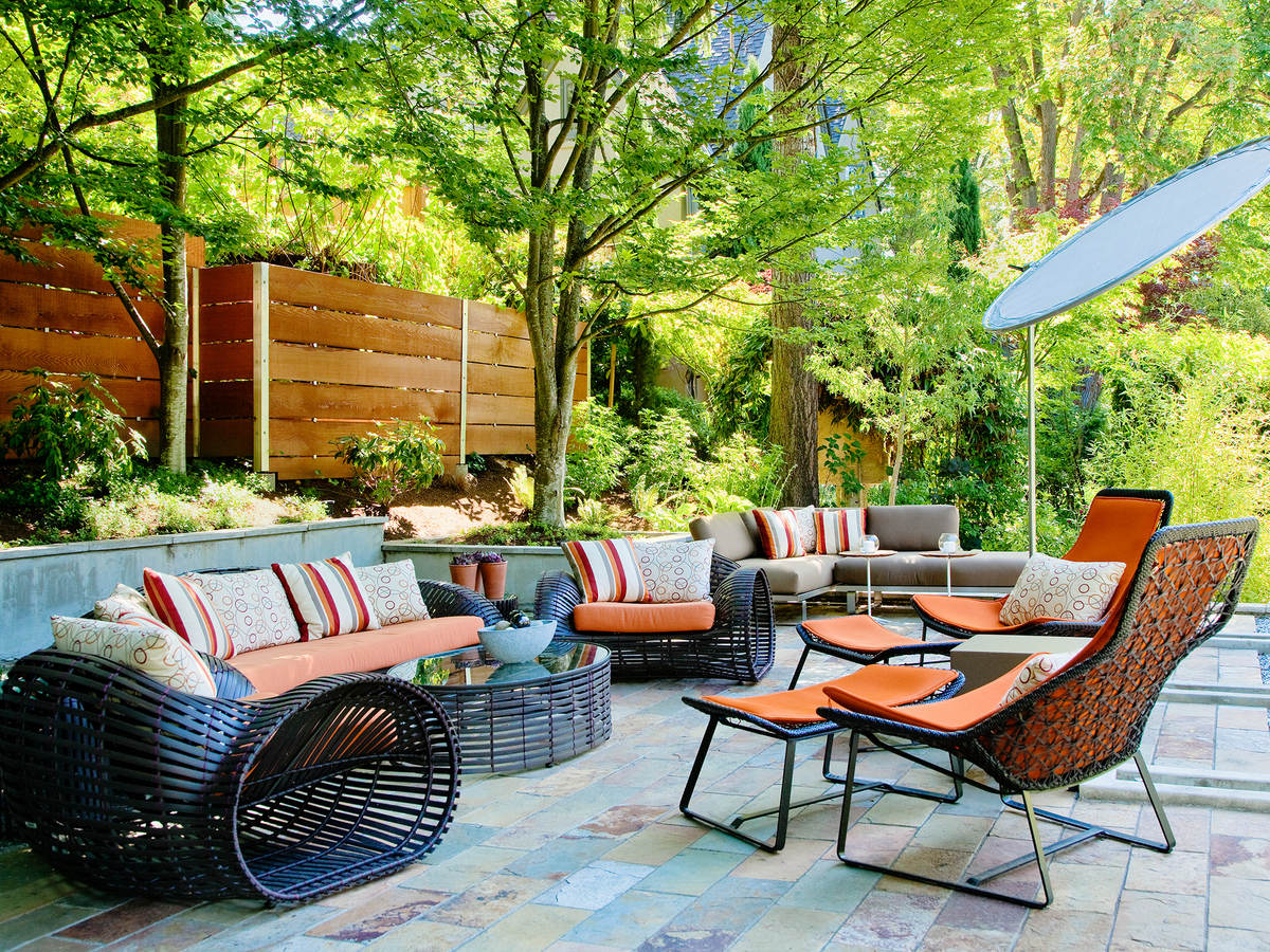 Outdoor furniture including sofa, chairs, table and umbrella in a sunny patio setting