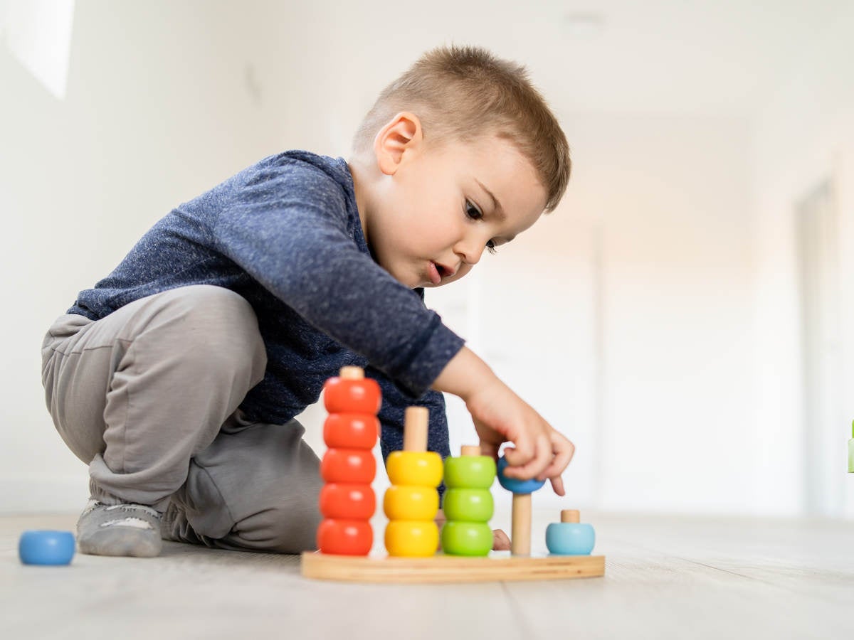 Small boy playing with little wood toys at home on the floor learning colors and counting