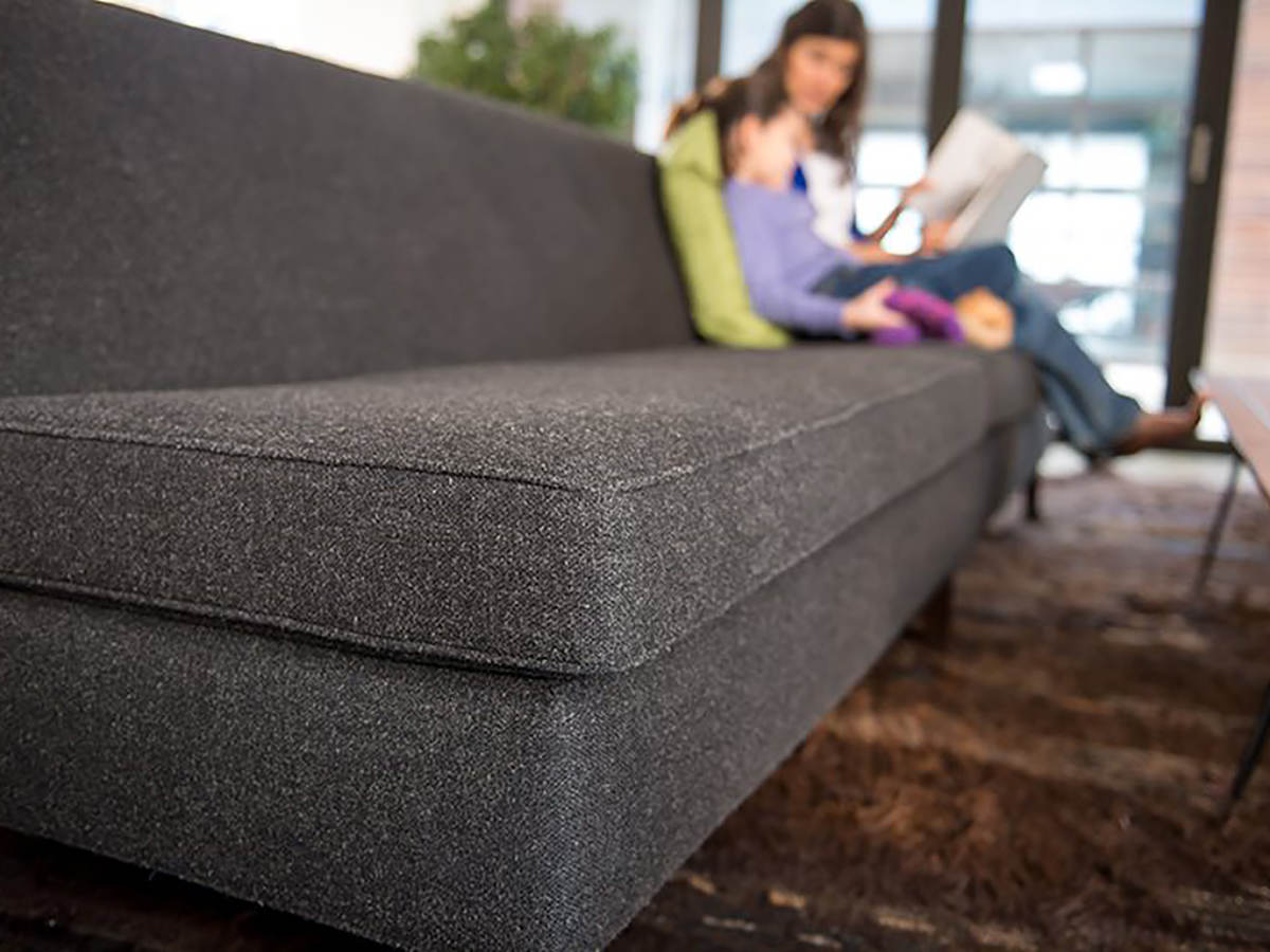 Woman and child comfortably sitting on a gray sofa, reading a book together