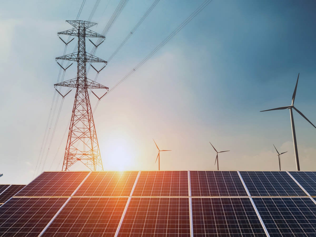 Large electric line tower over solar panels with sun in the background