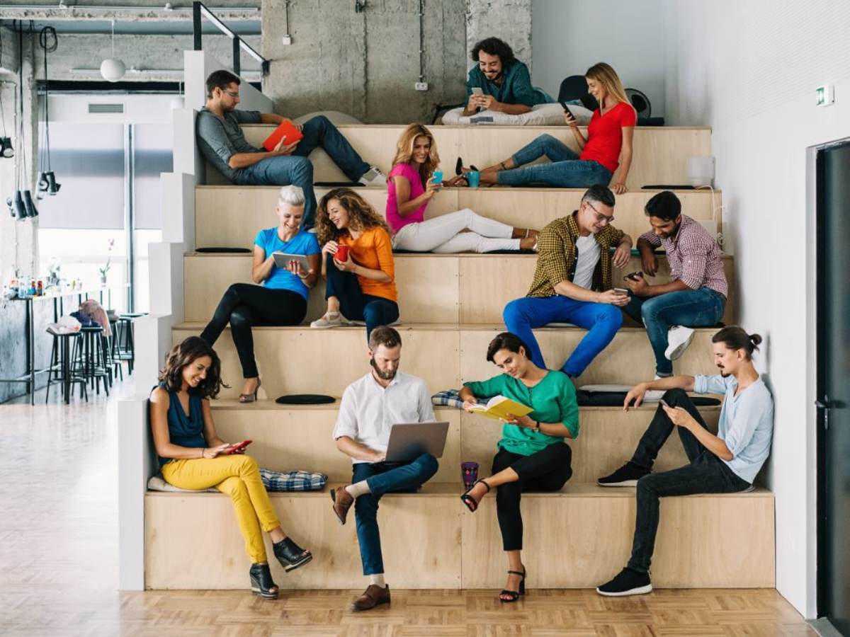 Group of young adults sitting on indoor tiered seating using their mobile phones and tablets.