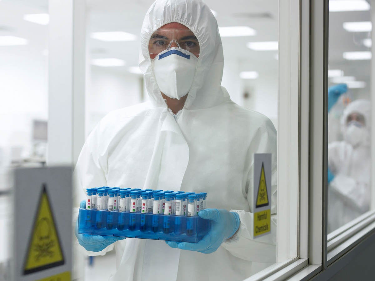 Person in PPE carrying tray of test tubes