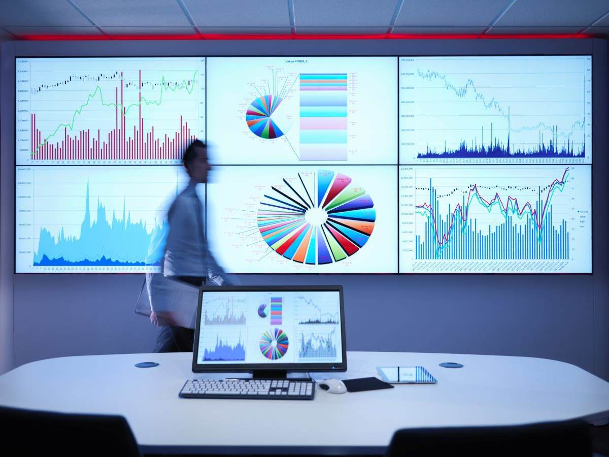 Man walking in front of large screen with multi-color pie chart and bar charts