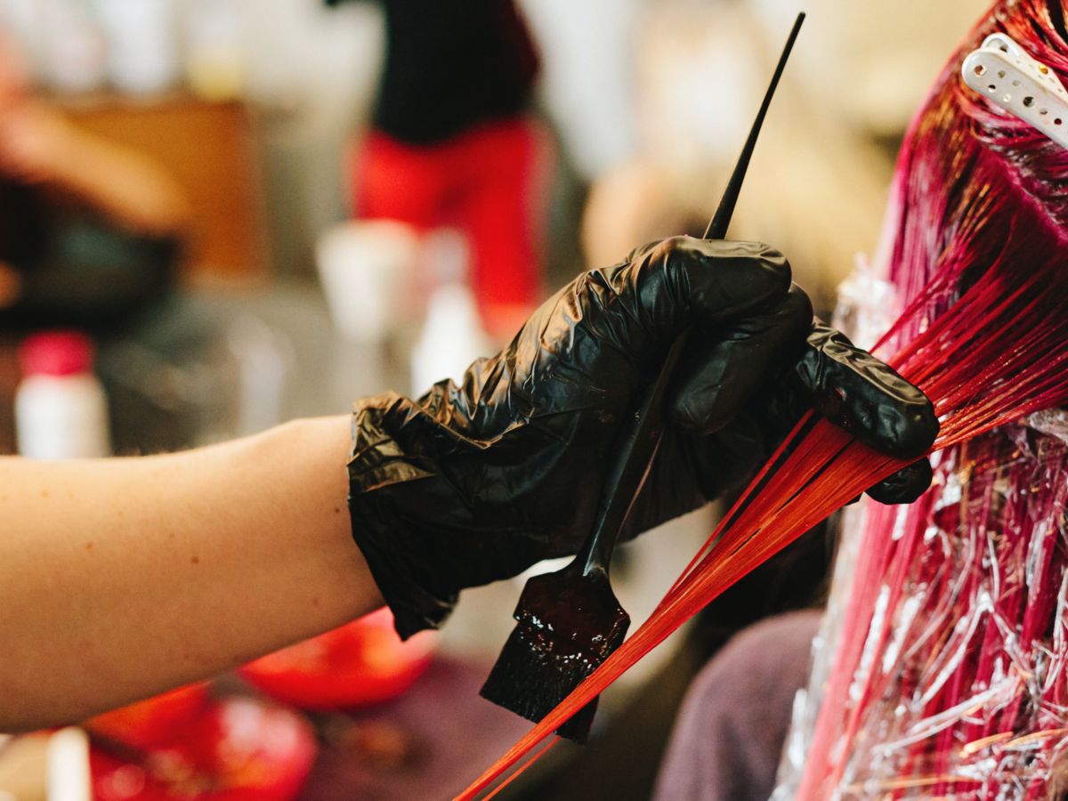 Black gloved hands putting pink dye in hair