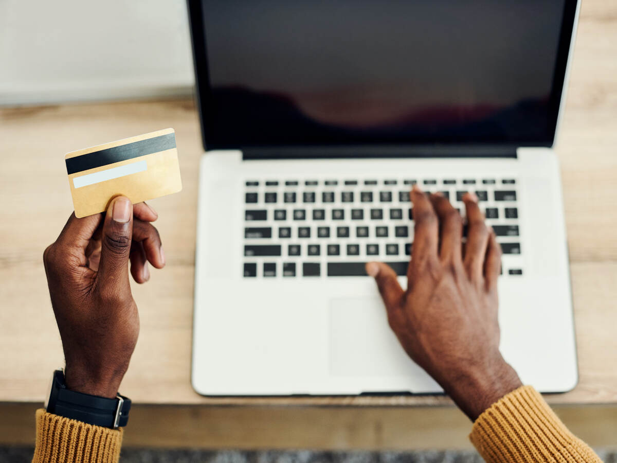 man looking at a credit card and typing on laptop keyboard