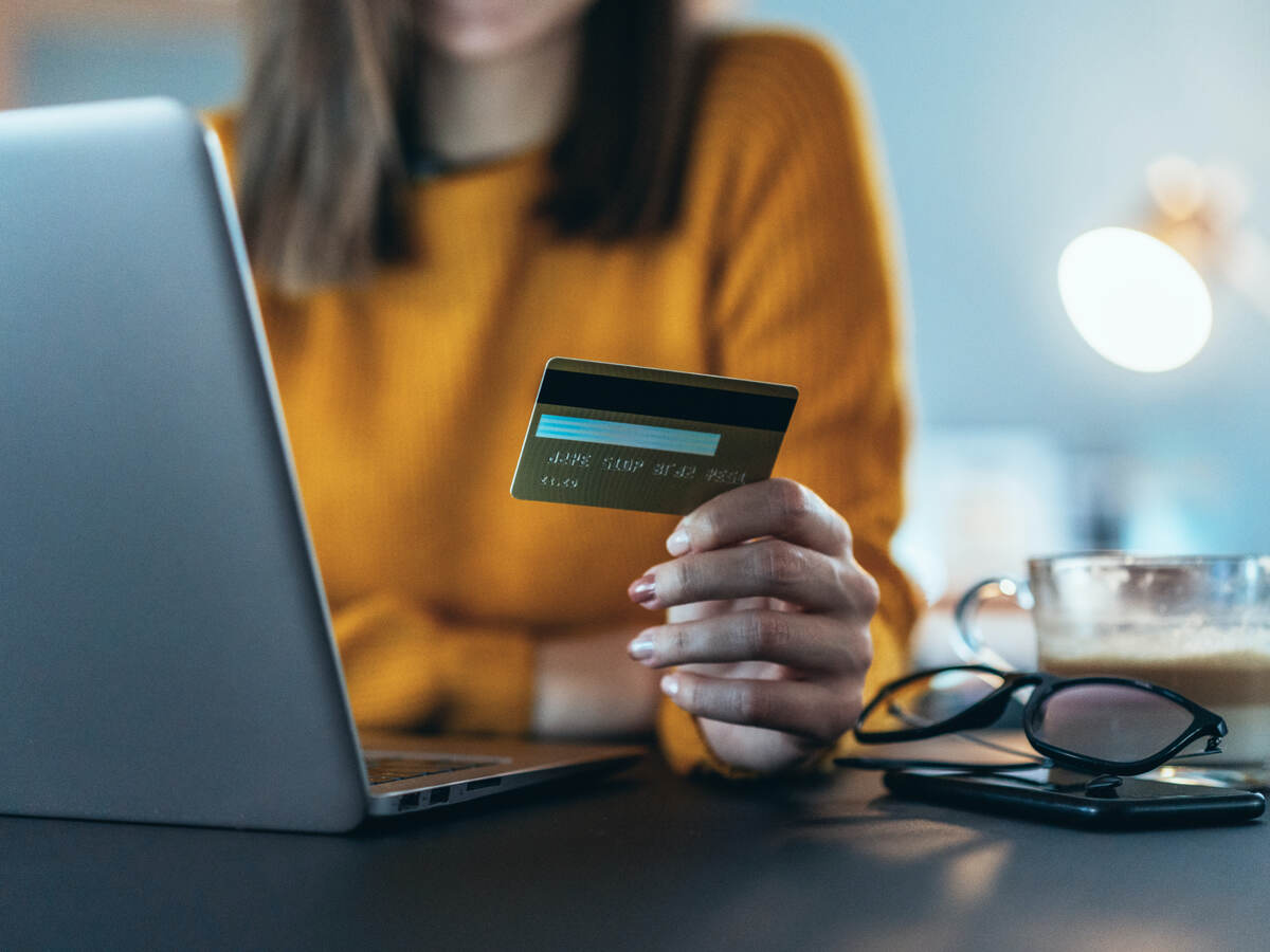 woman holding a credit card and sitting in front of a laptop computer