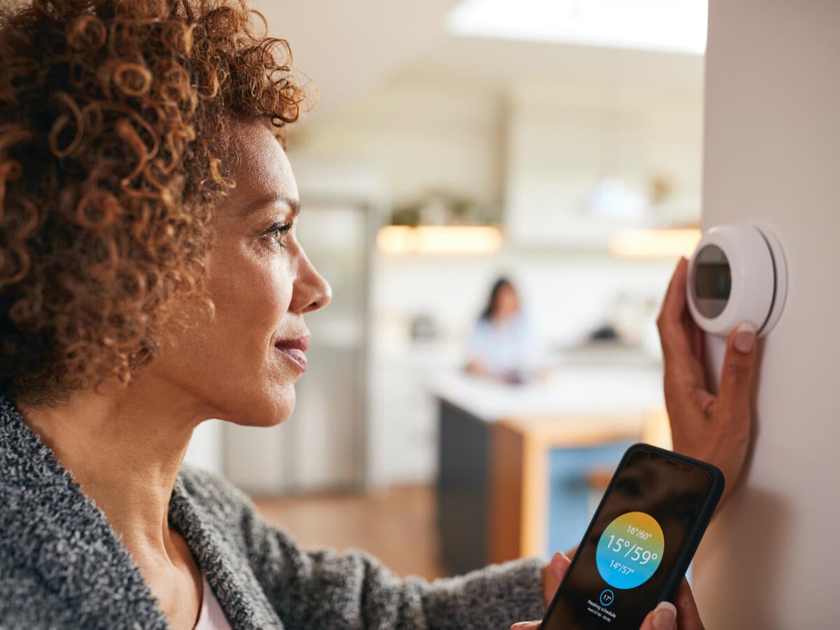 woman using app on mobile phone to control heating system at home