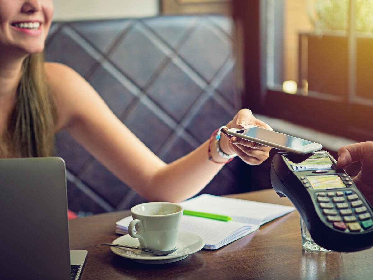 woman tapping a mobile phone for payment in cafe