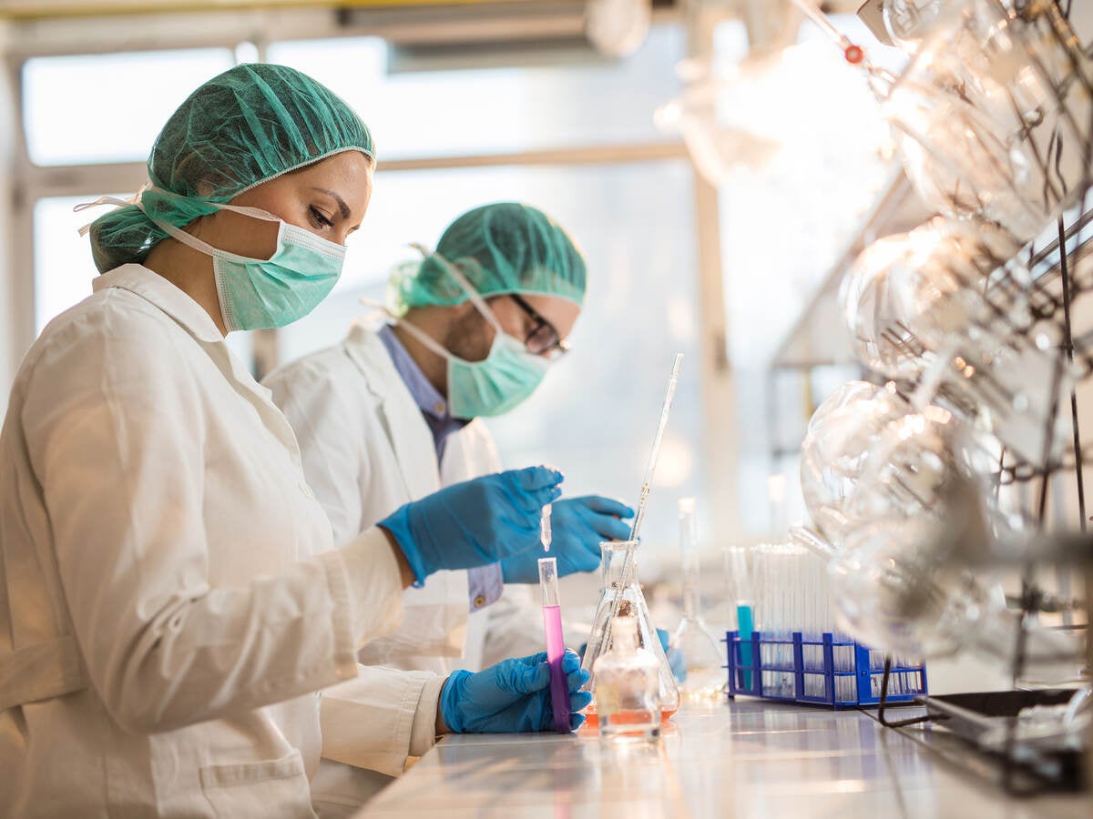 Two scientists wearing facemasks and examining chemical substances in test tubes in a laboratory.