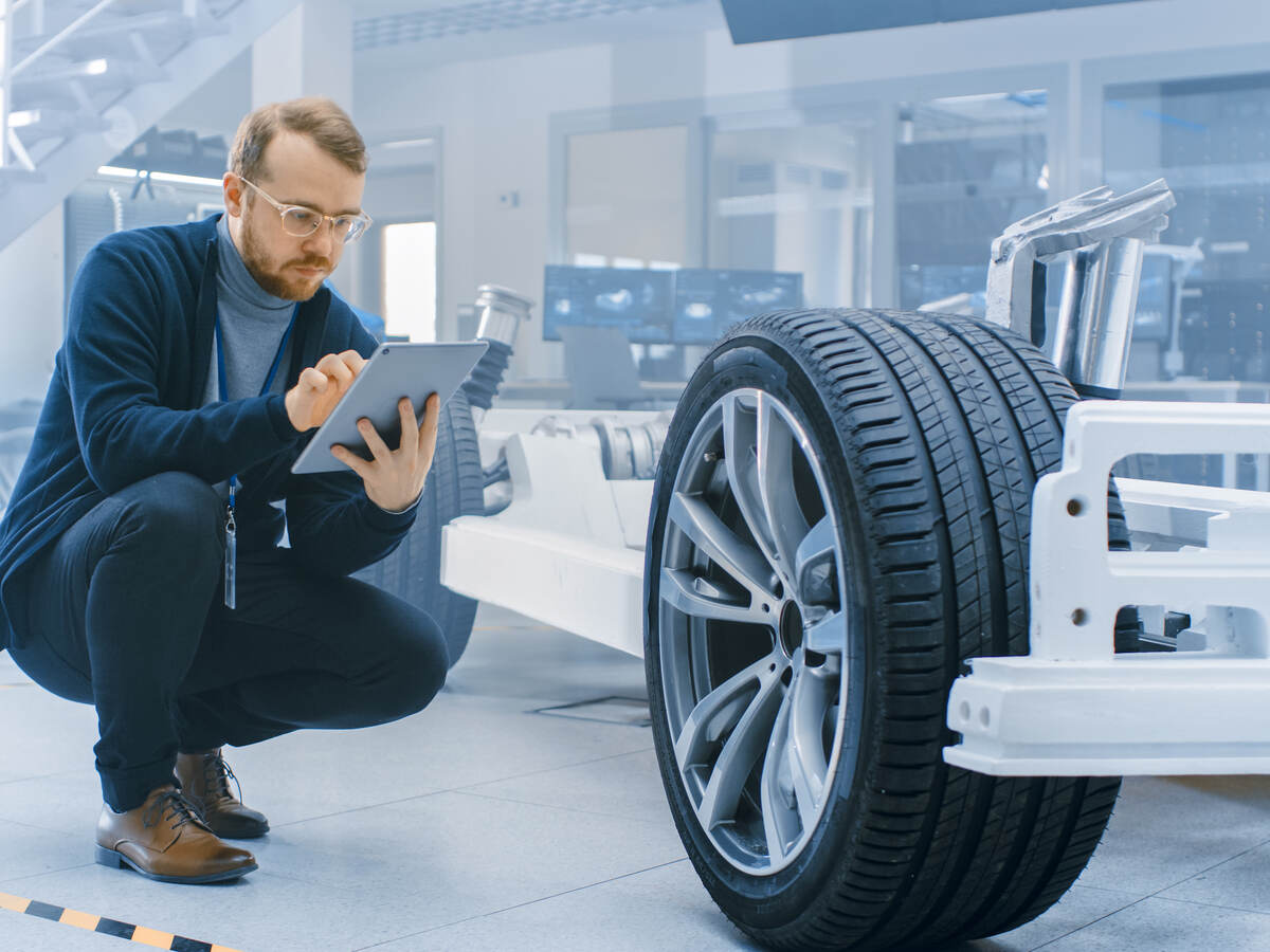 Engineer in an automotive laboratory works on a tablet and evaluates a car prototype