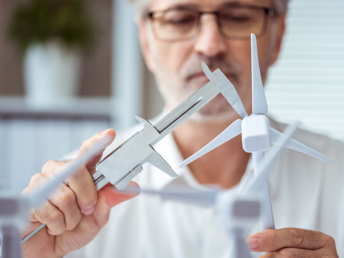 Person measuring a scale model of a wind turbine with calipers