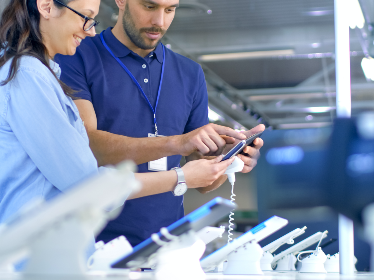 Electronics store employee shows a woman a new device.