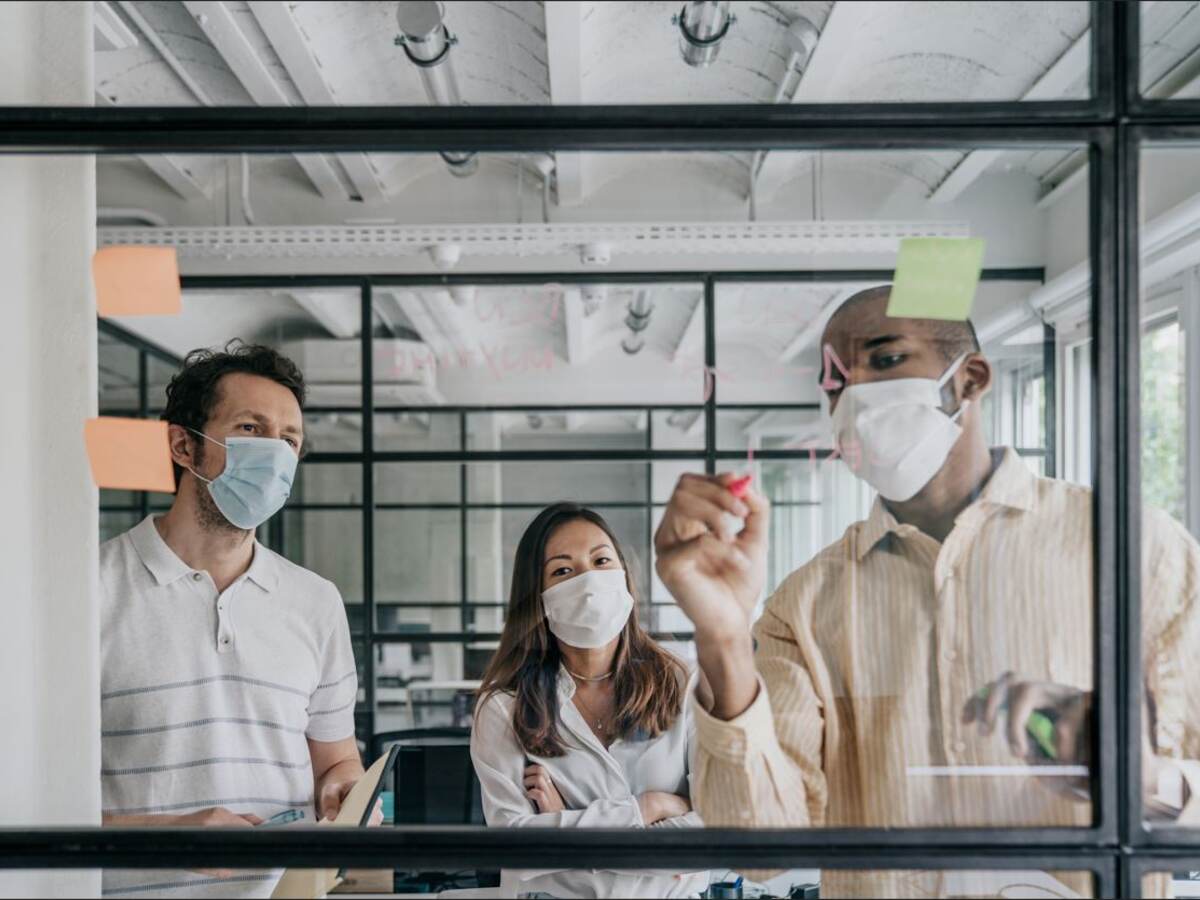 A man, a woman and another man collaborate on the other side of a transparent work board