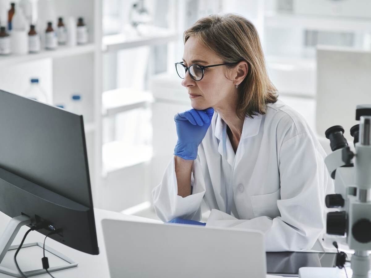 Woman in rubber gloves sitting at computer in lab