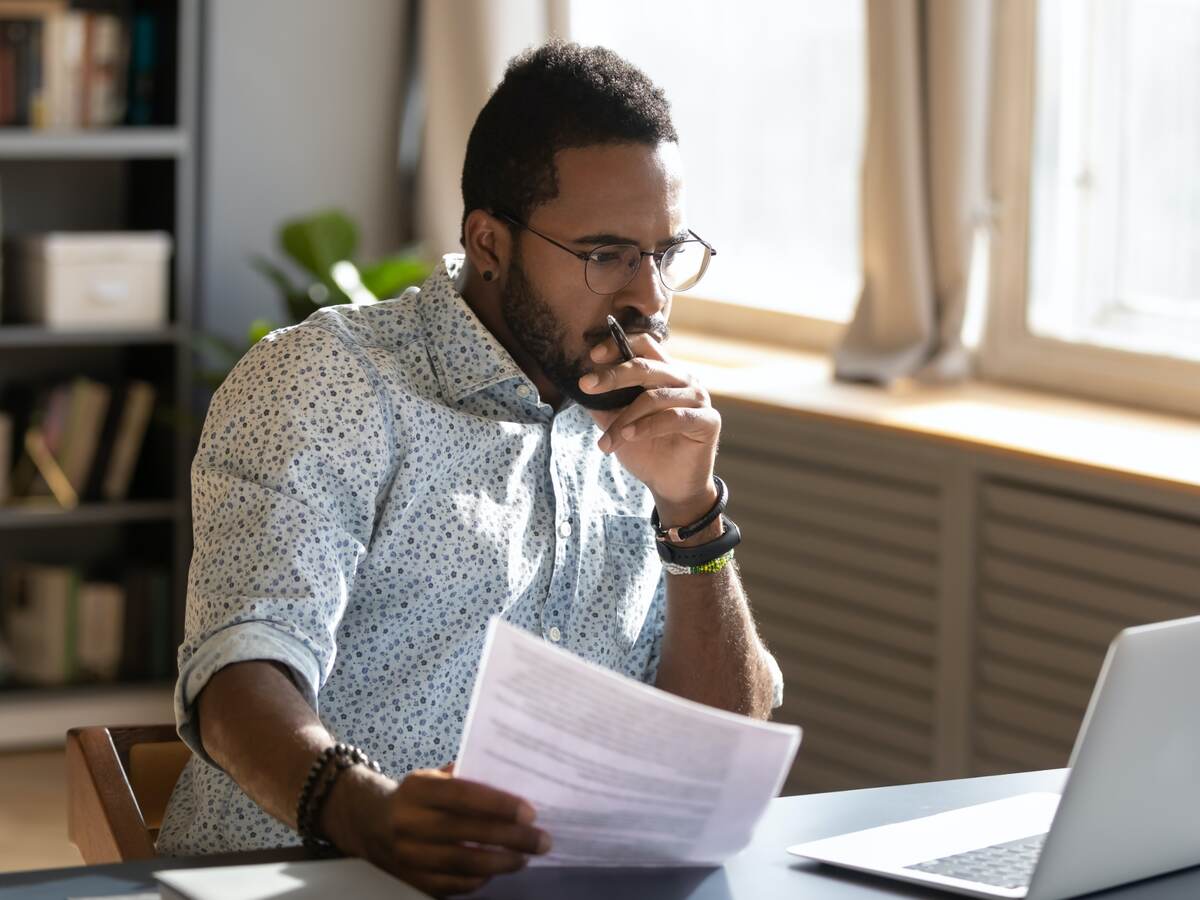 Person holding papers intensely looking at his open laptop