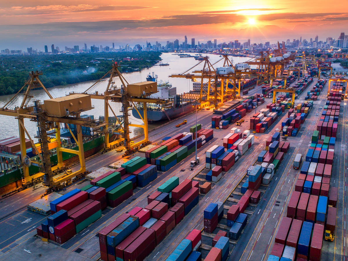 Container cargo ship and cargo plane with working crane bridge in shipyard at sunrise