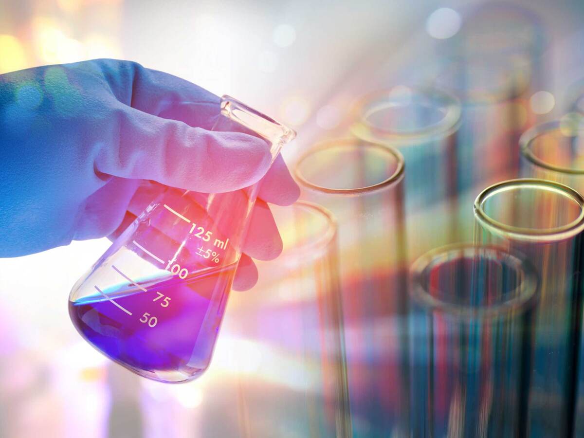 A gloved person pouring liquid from a beaker into test tubes