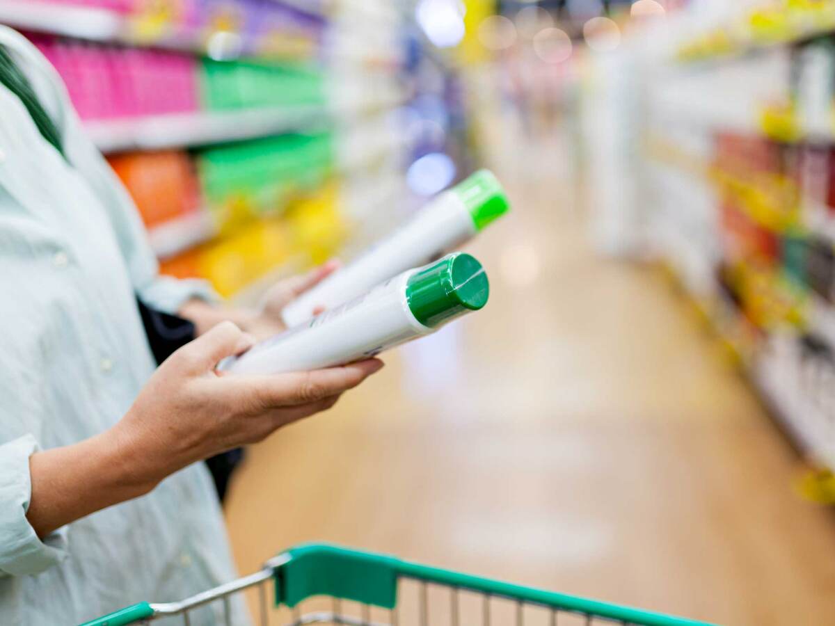 Person comparing green and white plastic bottles in a supermarket