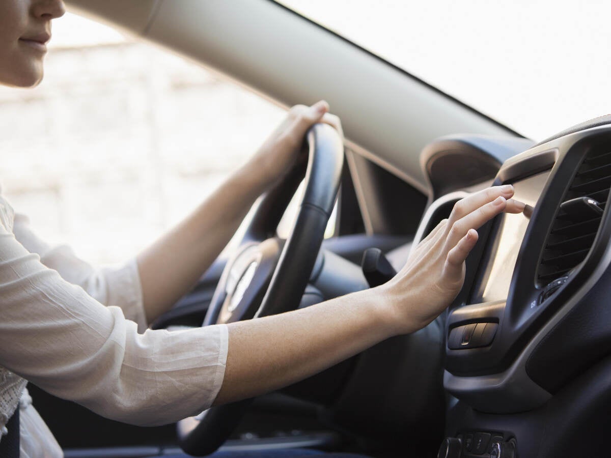 Woman in white shirt touches GPS screen on dashboard inside gray car. 