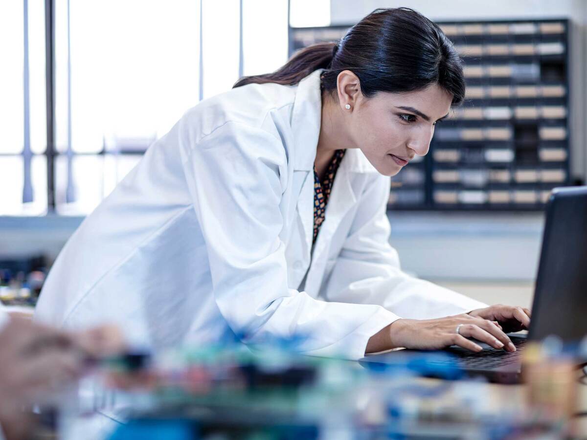 Person in white coat typing on lap top