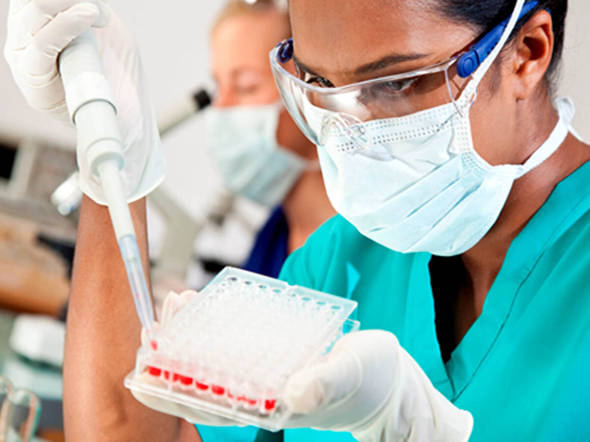 A lab worker in safety glasses and mask using large syringe to fill multicompartment test receptacle