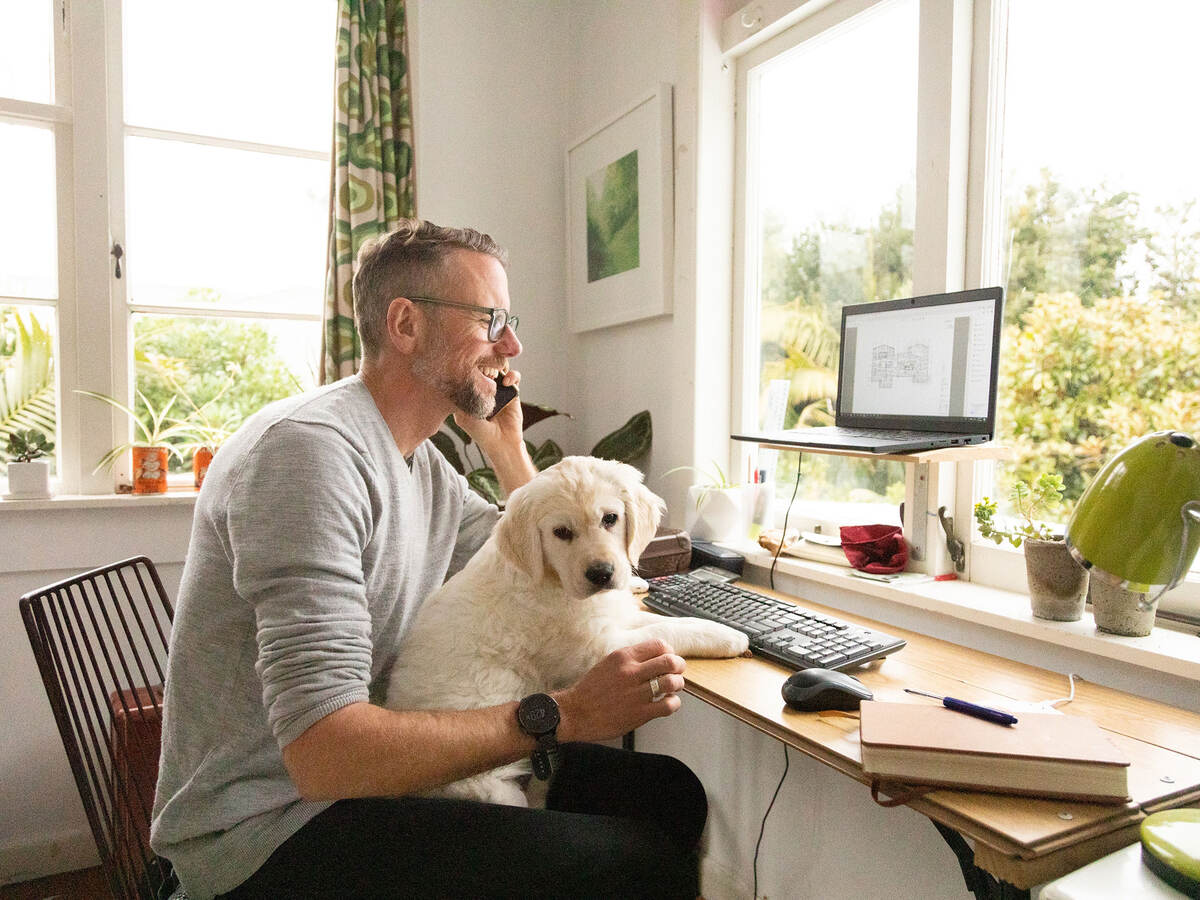 Person smiling and working from home with cute yellow puppy on their knee