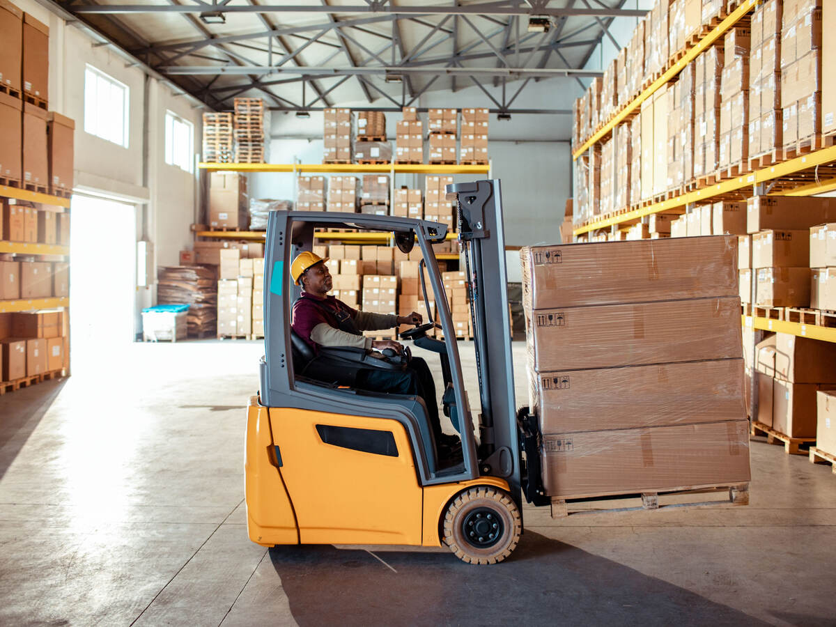 Worker using forklift to move boxes in a warehouse.