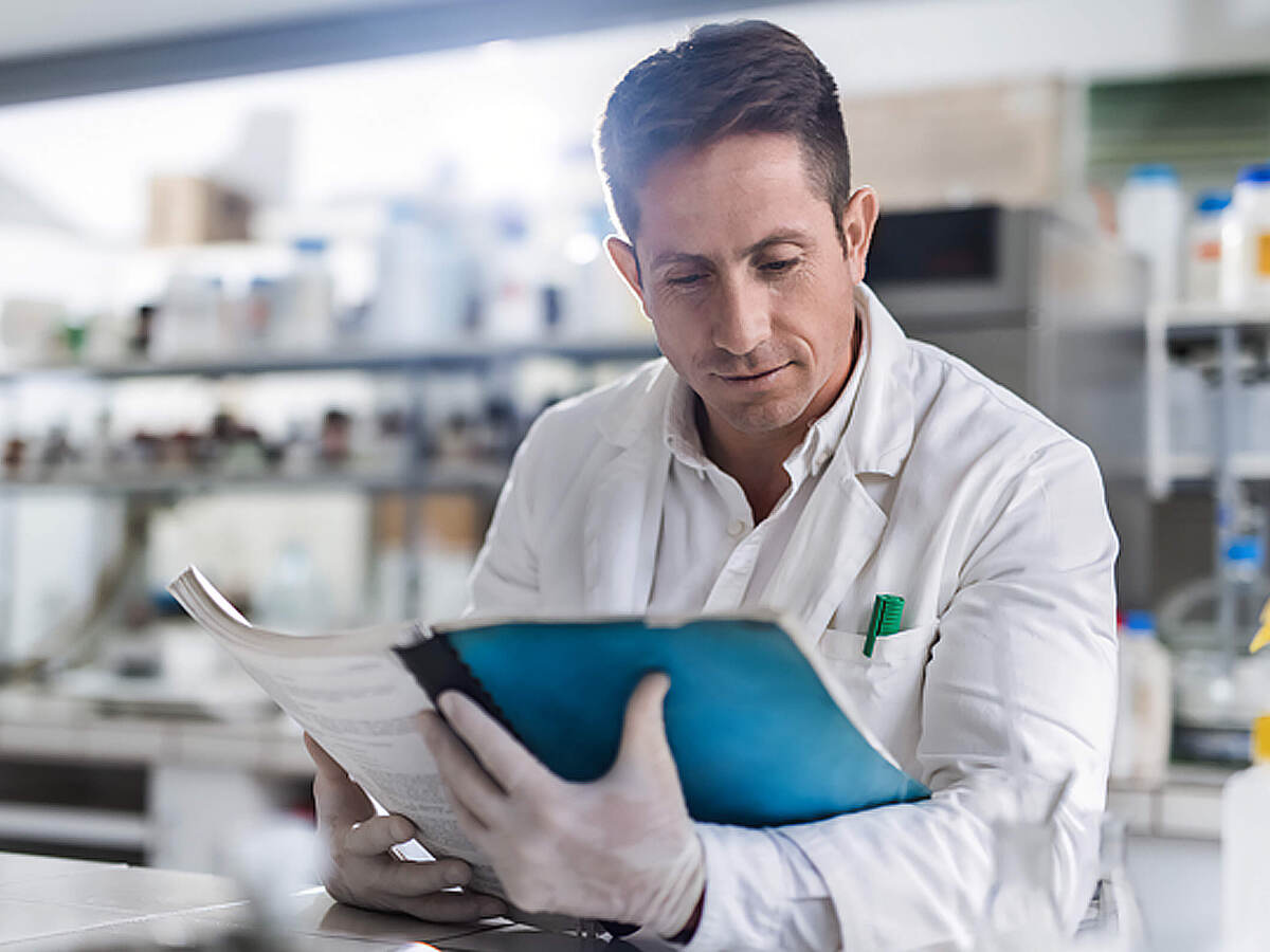 A laboratory worker sitting at a table reviews a guide