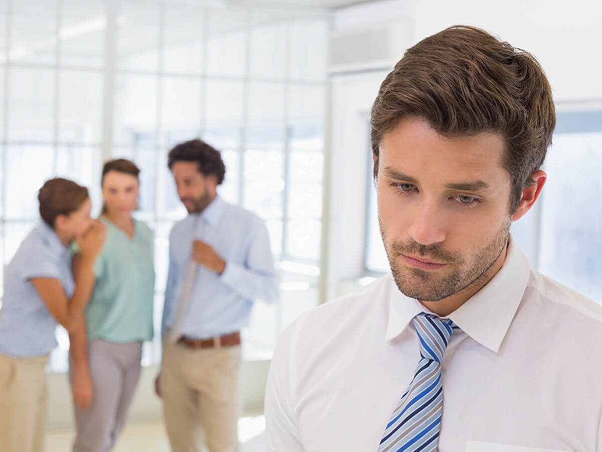 An employee in the foreground noticeably emotional while three coworkers whisper in the background