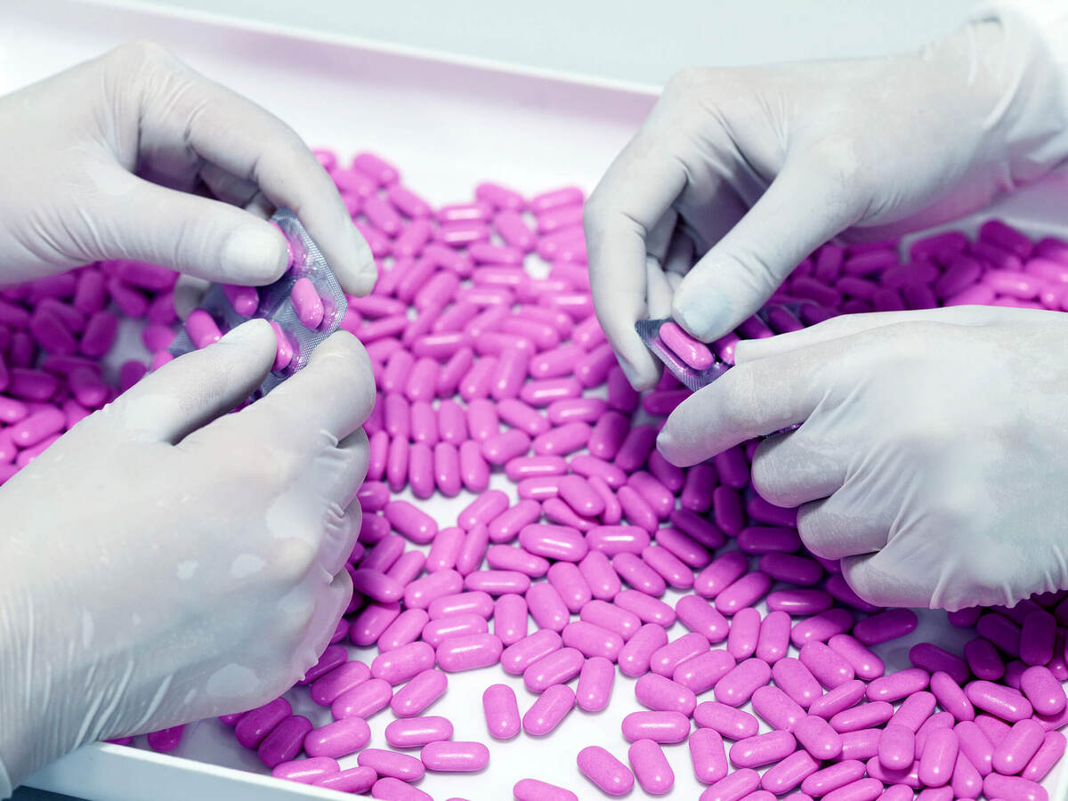 Two sets of hands in latex gloves remove purple pills from foil-backed medicinal packaging