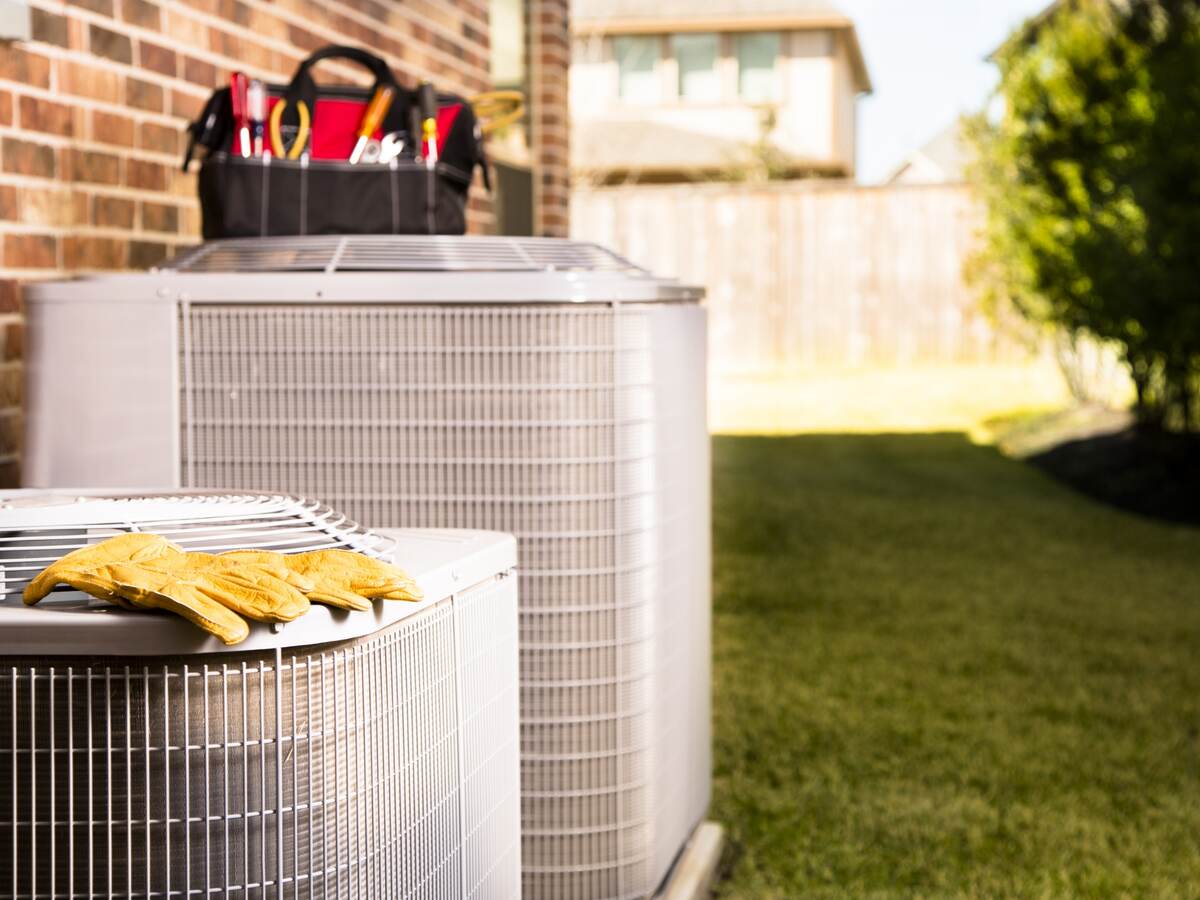 Bag of repairman’s work tools on top of air conditioner unit outside of residential home.