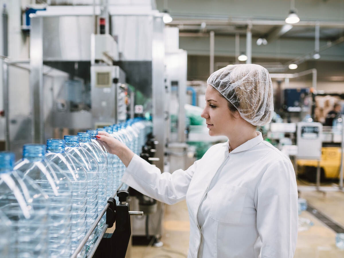 person inspecting conveyor belt of plastic water bottles