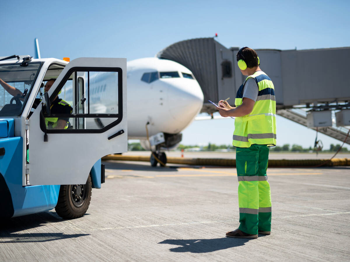 Worker taking notes at airfield while colleague sits in tug cab