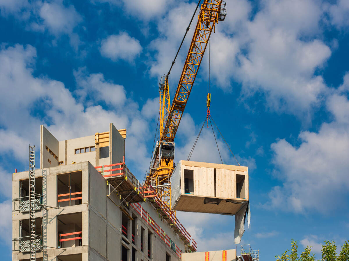 Crane lifting a prefabricated wooden building module to its position in the structure