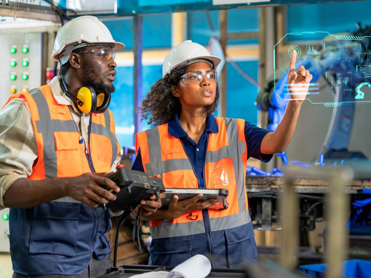 Engineer using tablet to check the robot system while her teamwork checks the security of the robot.