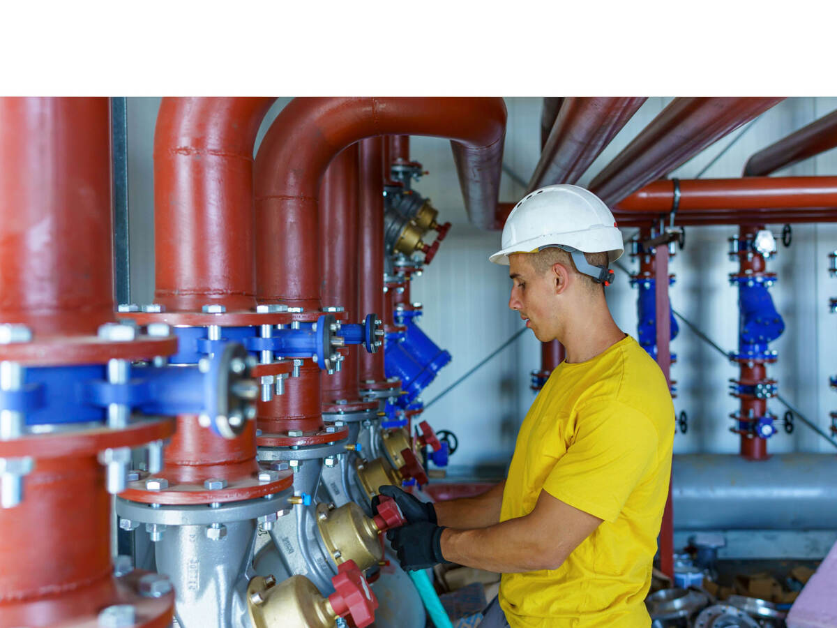 A male heating plant worker wearing a hardhat is standing next to a pipe system and performing a quality check.