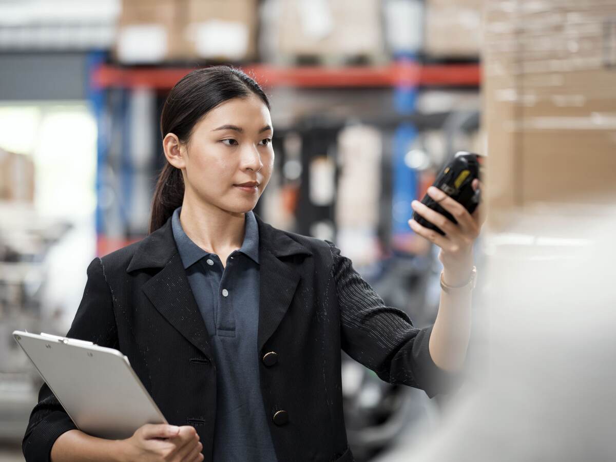 Asian Woman worker working in a modern distribution warehouse. Female warehouse staff uses a barcode reader to scan a product inside boxes on a shelf rack to receive into an inventory system.
