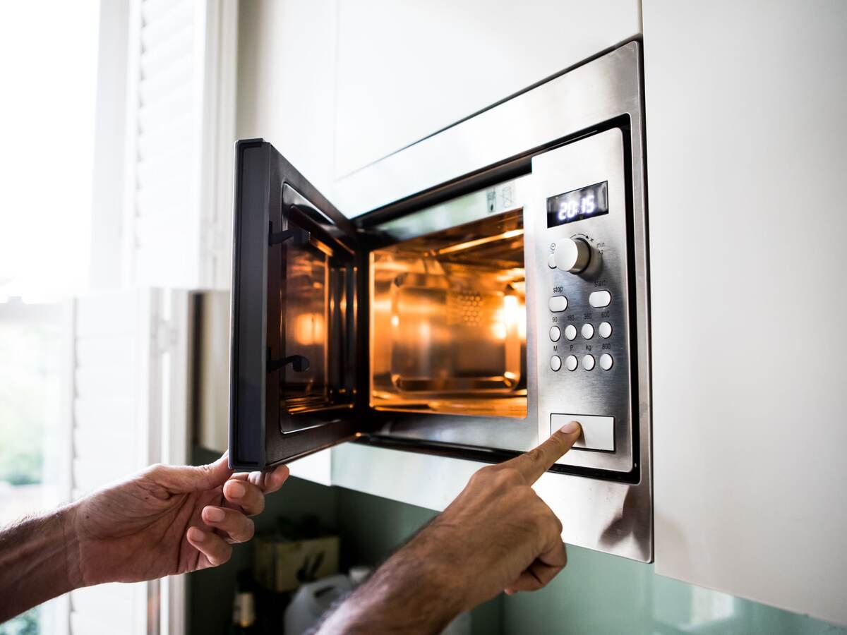 A man using a microwave oven. His finger on the opening button.