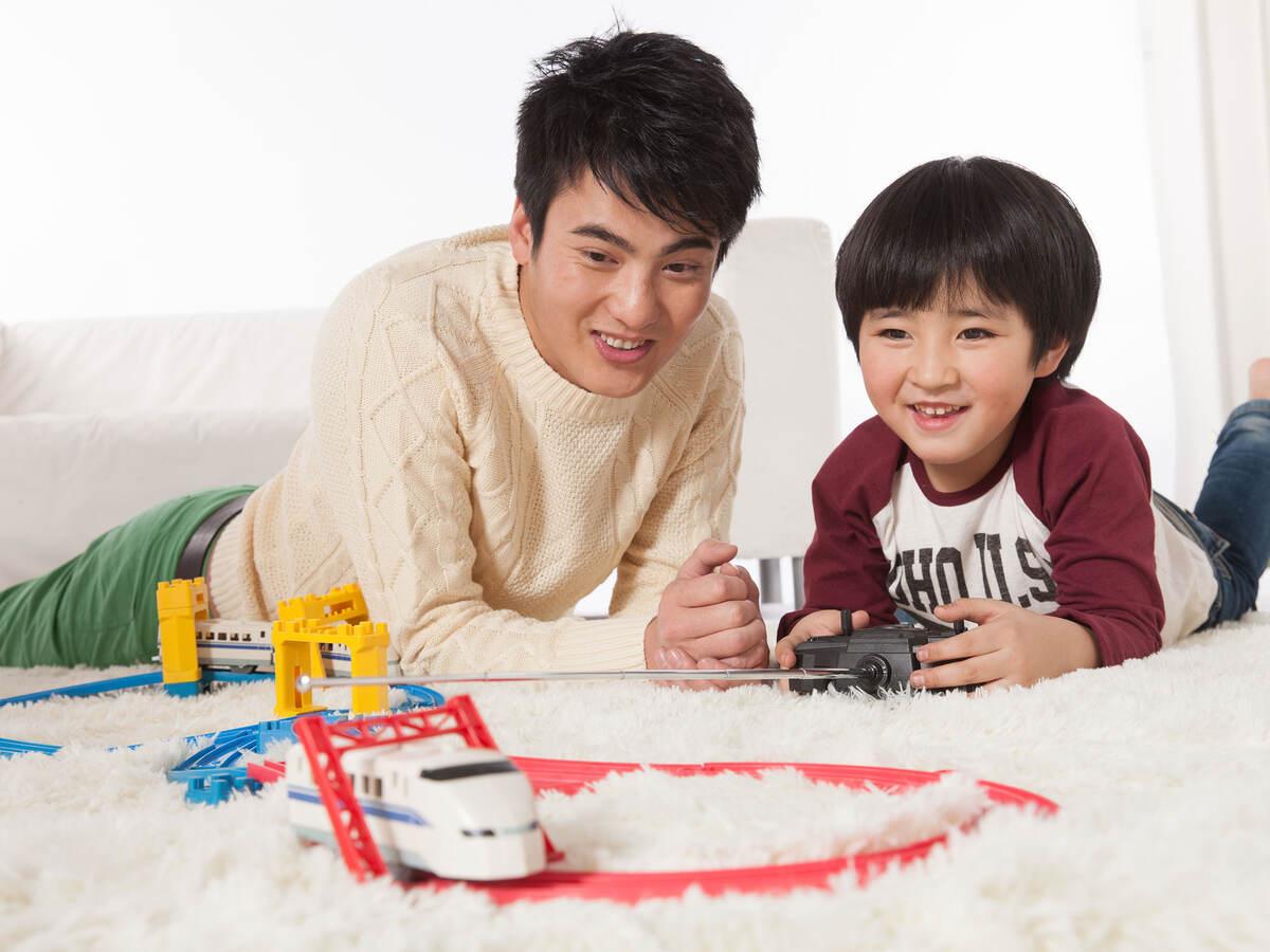 father and son on floor playing with toy train