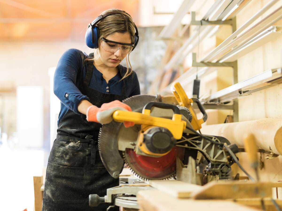 A female carpenter using a circular saw in a woodshop.