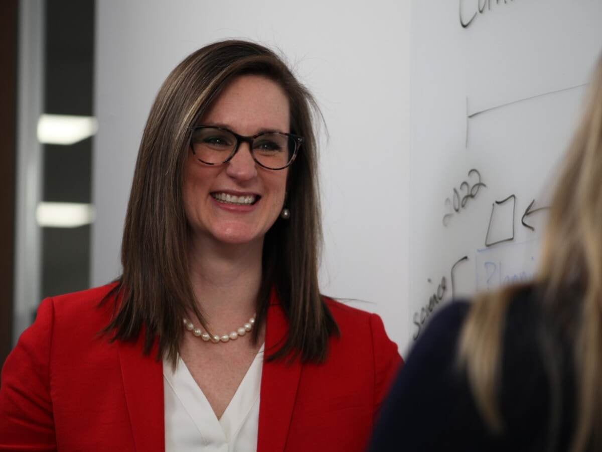 Melissa Albrecht in red jacket and white shirt smiles while talking to colleague. 